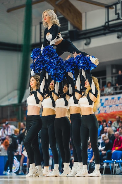 Photo cheerleader doing a split while other girls holding her up in the air on the basketball court