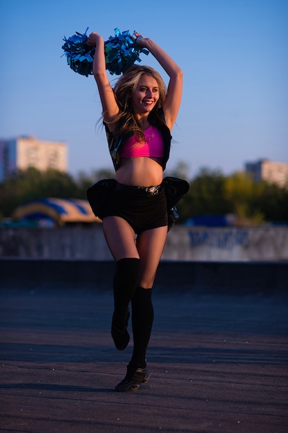 Cheerleader met pompoms die in openlucht op het dak bij zonsondergang dansen