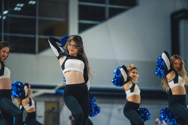 Foto cheerleaders in het zwart-witte uniform dansen met pompons binnen op een speelveld