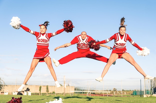 Photo cheerleaders performing with sportsman on field against blue sky