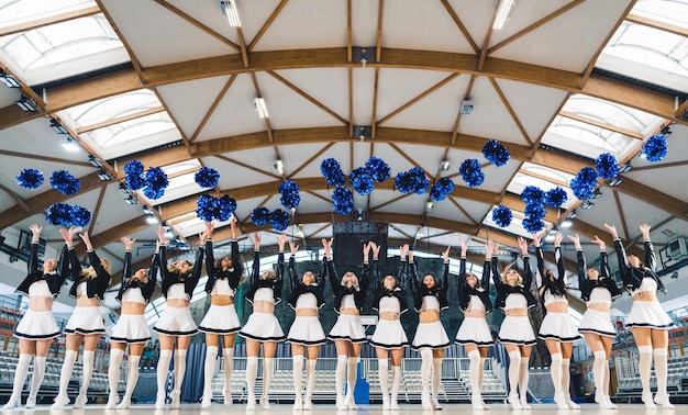 Foto cheerleaders staan in de rij en gooien pompons in de lucht op een basketbalveld