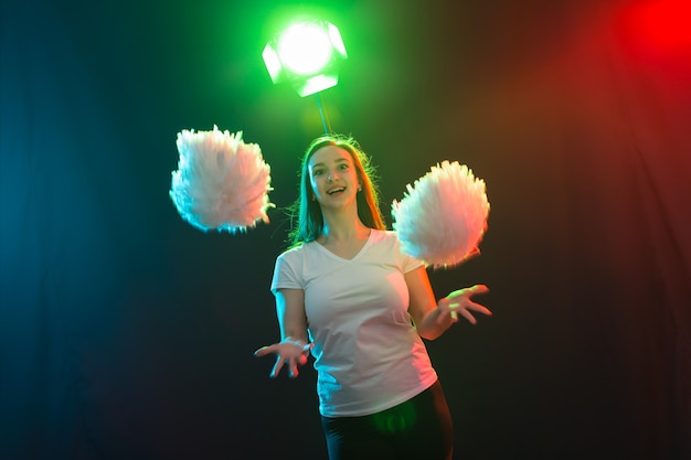 Cheerleading jonge vrouw dansen met pom-poms op kleurrijke achtergrond.