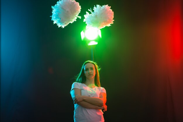 Cheerleading jonge vrouw dansen met pom-poms op kleurrijke achtergrond.