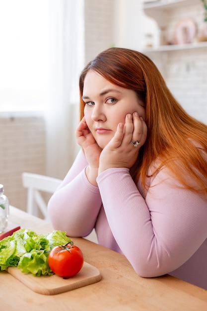 Безрадостная пухлая женщина думает о своей диете, готовясь сделать салат