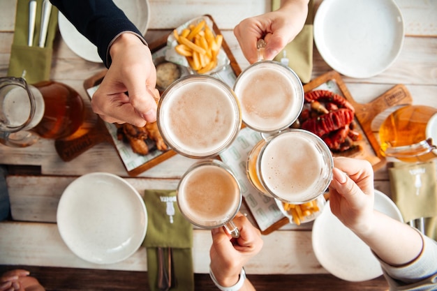 テーブルの上にビールとマグカップを持っている手を乾杯