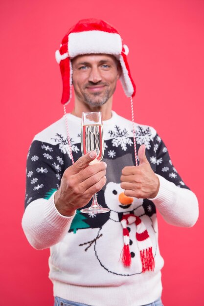 Cheers. Handsome man celebrate winter holidays red background. Guy wear winter sweater. Merry christmas and happy new year. Best wishes. Winter vacation. Sparkling wine selective focus close up.