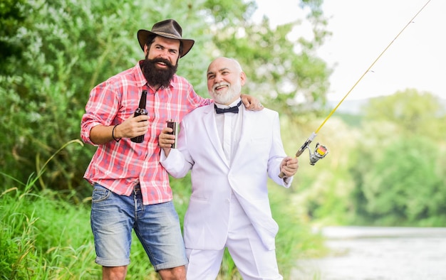 Cheers Men relaxing nature background Fun and relax Weekend time Fishing skills Set up rod with hook line sinker Fishing and drinking beer Bearded man and elegant businessman fishing together