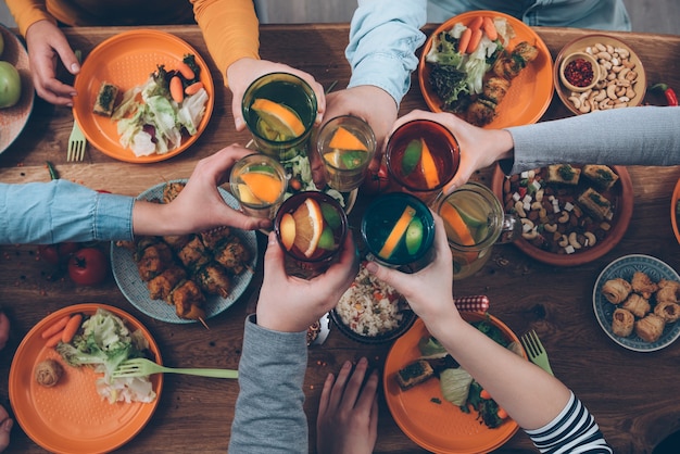 Cheers! Top view of people cheering with drinks while sitting at the rustic dining table