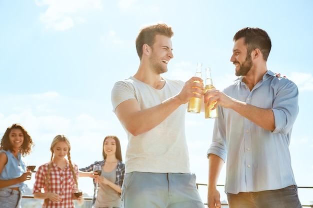 Cheers to us two smiling young men clinking glasses with beer and looking at each