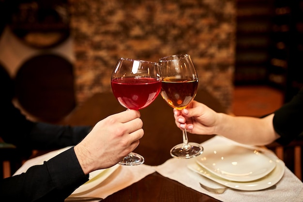 Saluti con bicchieri di vino primo piano coppia giovane innamorata ad un appuntamento in un ristorante il ragazzo e la ragazza riposano in un luogo accogliente e bevono vino