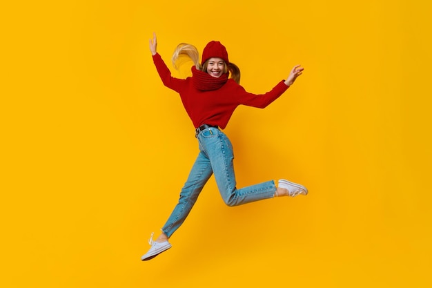 Cheery blonde winter girl having fun over yellow studio background