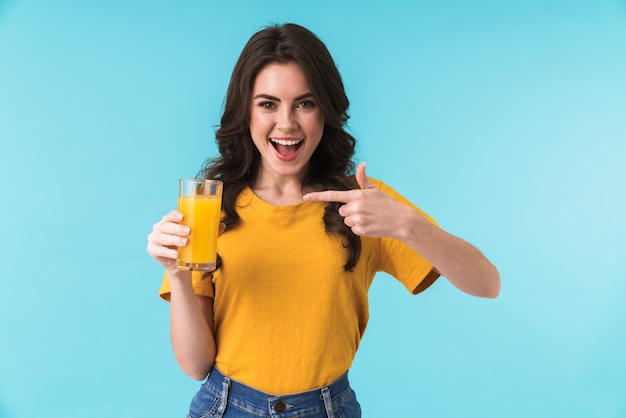 cheery happy woman posing isolated over blue wall holding juice pointing.