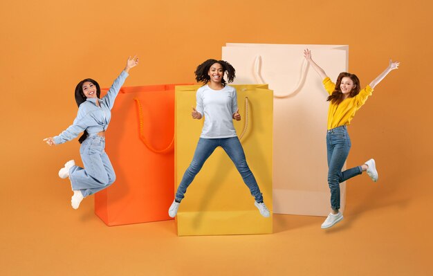 Cheery multiethnic young women jumping next to shopping bags