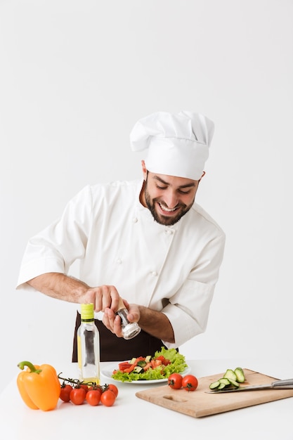 cheery pleased young chef in uniform cooking with fresh vegetables.