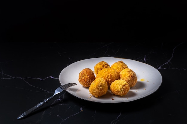 Photo cheese balls with garlic and dill inside for a snack in a white plate on a black background