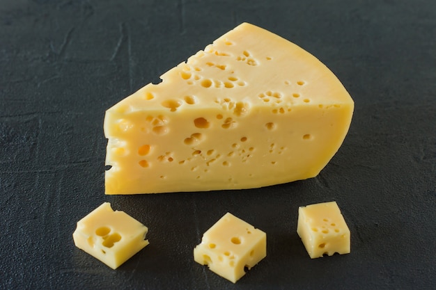 Cheese on a black concrete background. triangular piece of\
yellow cow\'s milk cheese with holes