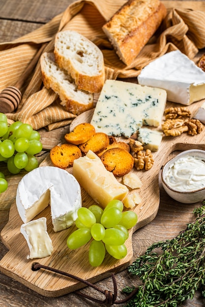 Cheese Board. Brie, Camembert, Roquefort, parmesan and blue cream cheese with grape, fig, bread and nuts on wooden board. wooden background. Top view.