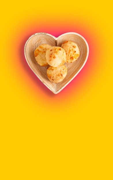 Cheese bread (Brazilian pao de queijo mineiro), top view, yellow background, on a heart shaped plate