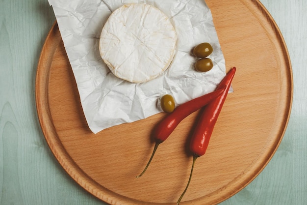cheese brie camembert green olives chili on a wooden light background vintage photo processing