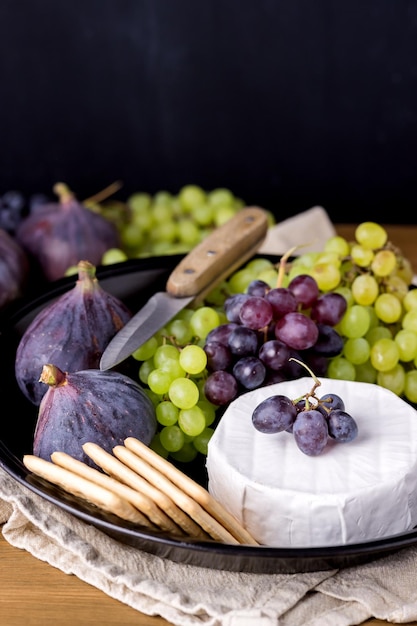 Cheese Brie Camembert with Figs and Grapes on wooden table Food for Wine Figs Green and Red Grapes Crackers Knife Plate Snacks Vertical