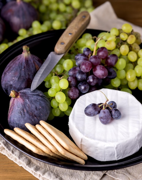 Cheese Brie Camembert with Figs and Grapes on wooden table Food for Wine Figs Green and Red Grapes Crackers Knife Plate Snacks Vertical Above