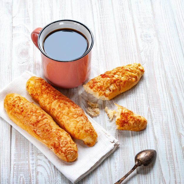 Cheese buns, bread with cheese and a cup of coffee with a spoon on a white wooden background