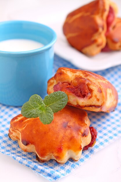 Cheese buns with cherry jam. Blue cup with milk. White background.