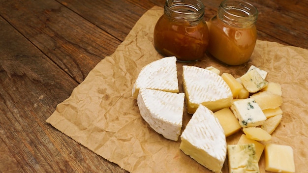 Cheese on craft paper with home made jam and honey in glass jar food concept