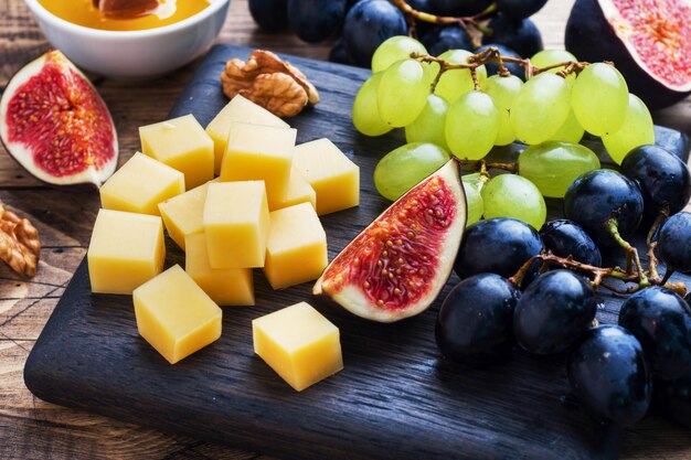 Cheese cubes, fresh fruit figs grapes Honey walnut on wooden chopping Board. Selective focus. Close up.