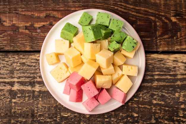 Кубики сыра зеленого, желтого и красного цвета на тарелке, закуска к вину. Посмотреть сверху. Закрыть вверх