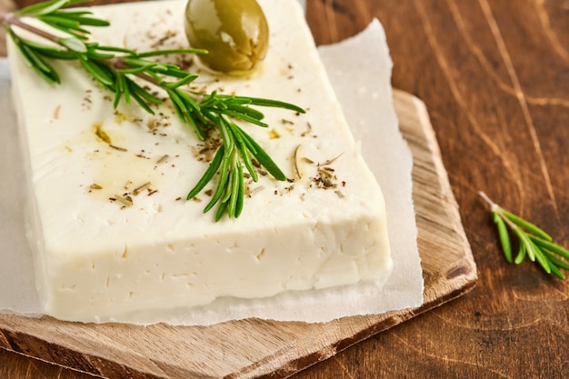 Cheese feta with rosemary, herbs, olives and olive oil on wooden cutting board on old wooden surface