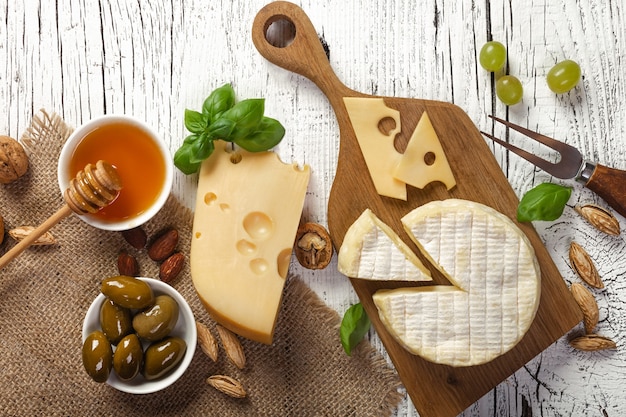 白い木製のテーブルにチーズ、ブドウ、蜂蜜、ナッツ。上面図。