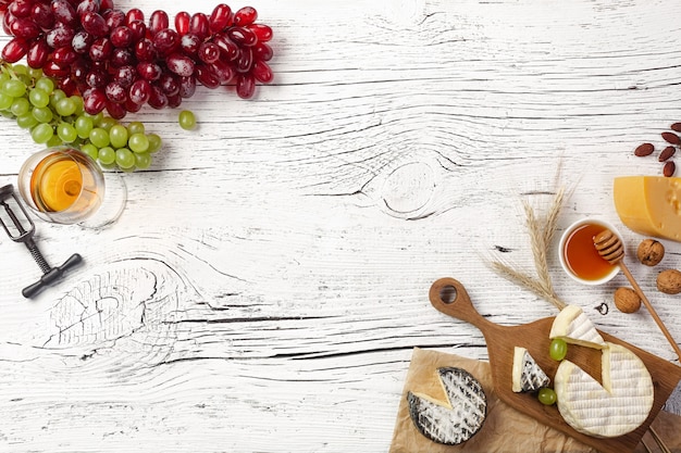 Cheese, honey, grape, nuts and wineglass on white wooden board