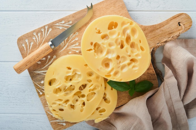 Cheese maasdam or radamer piece of cheese on wooden stand board\
on white wooden table background top view free space for your\
text