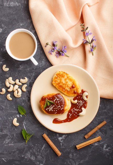 Frittelle al formaggio con salsa al caramello su un piatto in ceramica beige e una tazza di caffè su cemento nero