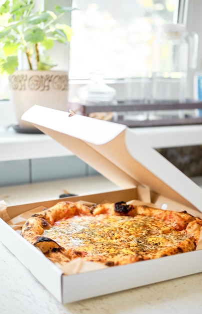 Cheese pizza in an ajar box on a white table by the window Order food home