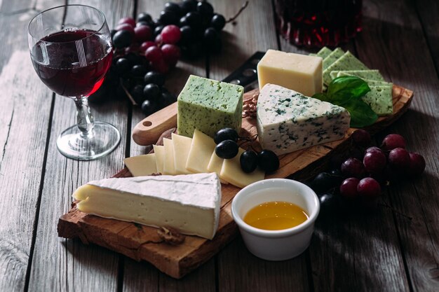 Cheese plate on a dark background. Brie, dor blue, gouda, grapes, nuts, wine