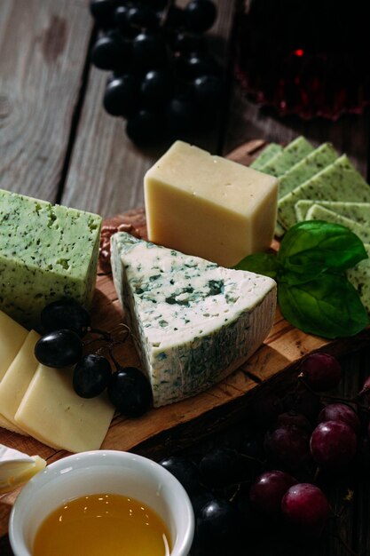 Cheese plate on a dark background. Brie, dor blue, gouda, grapes, nuts, wine