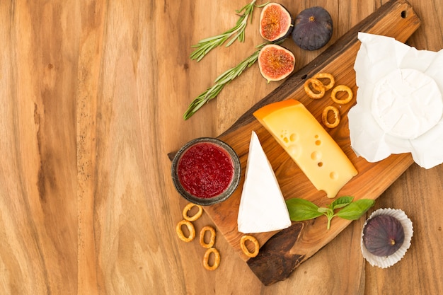 Cheese plate served with jam, figs, crackers and herbs on a wooden background.