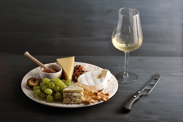 Cheese plate, wine and cheese knife on dark