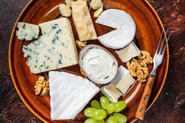 Cheese plate with Brie, Camembert, Roquefort, blue cream cheese, grape and nuts. Dark background. Top view.