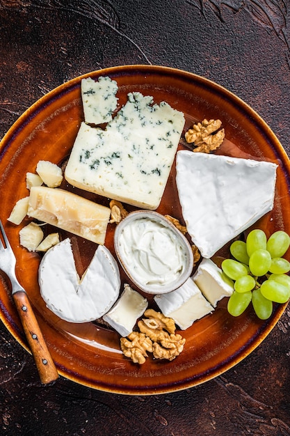 Cheese plate with Brie, Camembert, Roquefort, blue cream cheese, grape and nuts. Dark background. Top view.