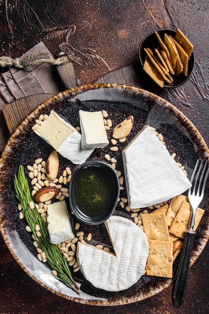 Cheese plate with brie and camembert on rustic plate with nuts and honey. Dark background. Top view.