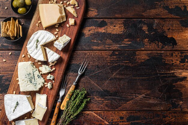 Cheese plate with camembert, brie, gorgonzola, parmesan,\
olives, nuts and crackers. wooden background. top view. copy\
space.