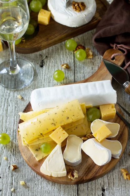 Piatto di formaggi con uva, bicchiere di vino e noci su un tavolo di legno.