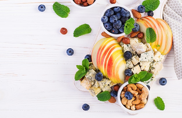 Photo cheese platter with assorted cheeses, blueberry, apples, nuts on white table. italian cheese  platter and fruit. top view, overhead