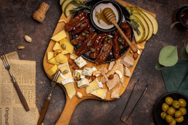 Cheese platter with different cheeses, dried tomatoes, nuts, honey and dates on rustic wooden board.