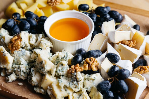 Cheese platter with grapes nuts and honey on wooden board