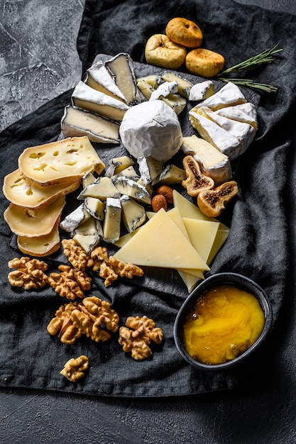 Cheese platter with organic cheeses, figs, nuts on black\
background. top view. tasty cheese starter