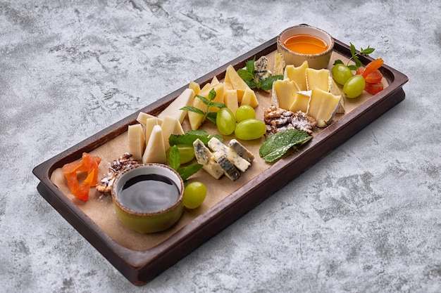 Cheese platter on a wooden board with grapes, mint, honey and jam